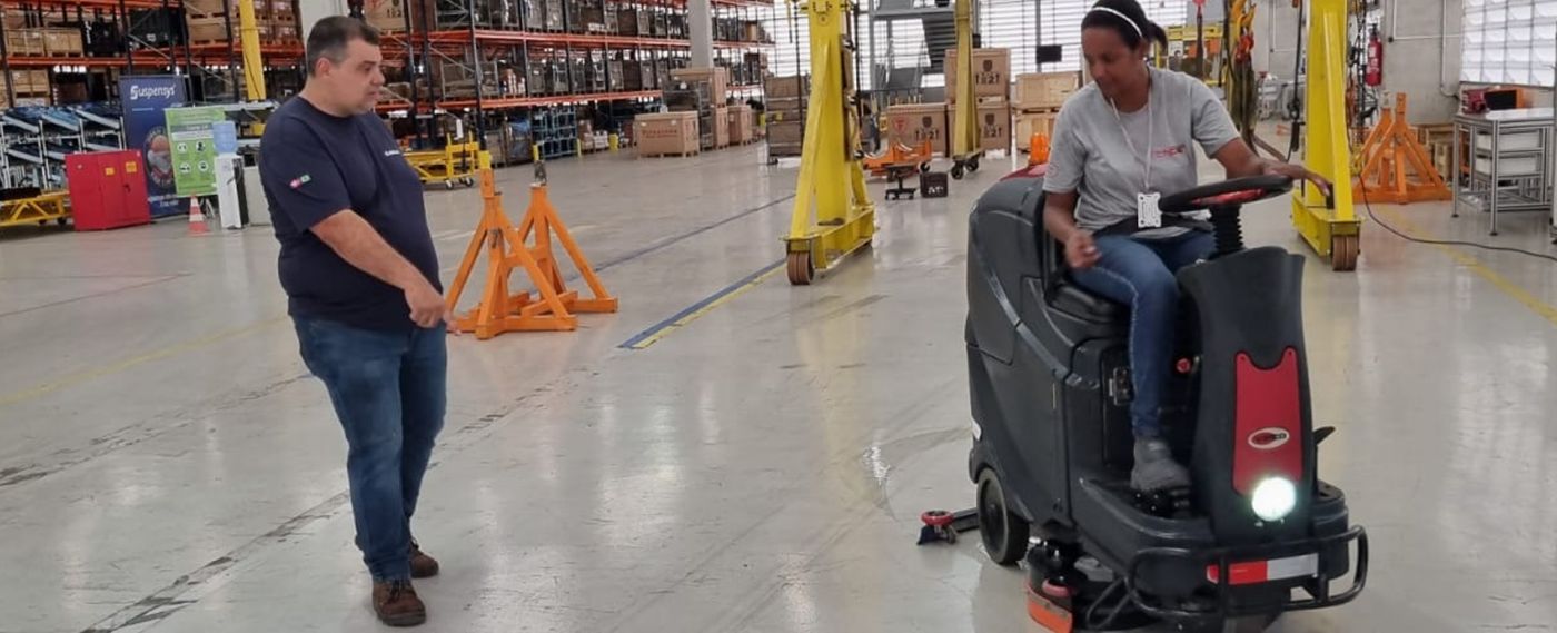 Operadora conduzindo lavadora de piso em galpão logístico